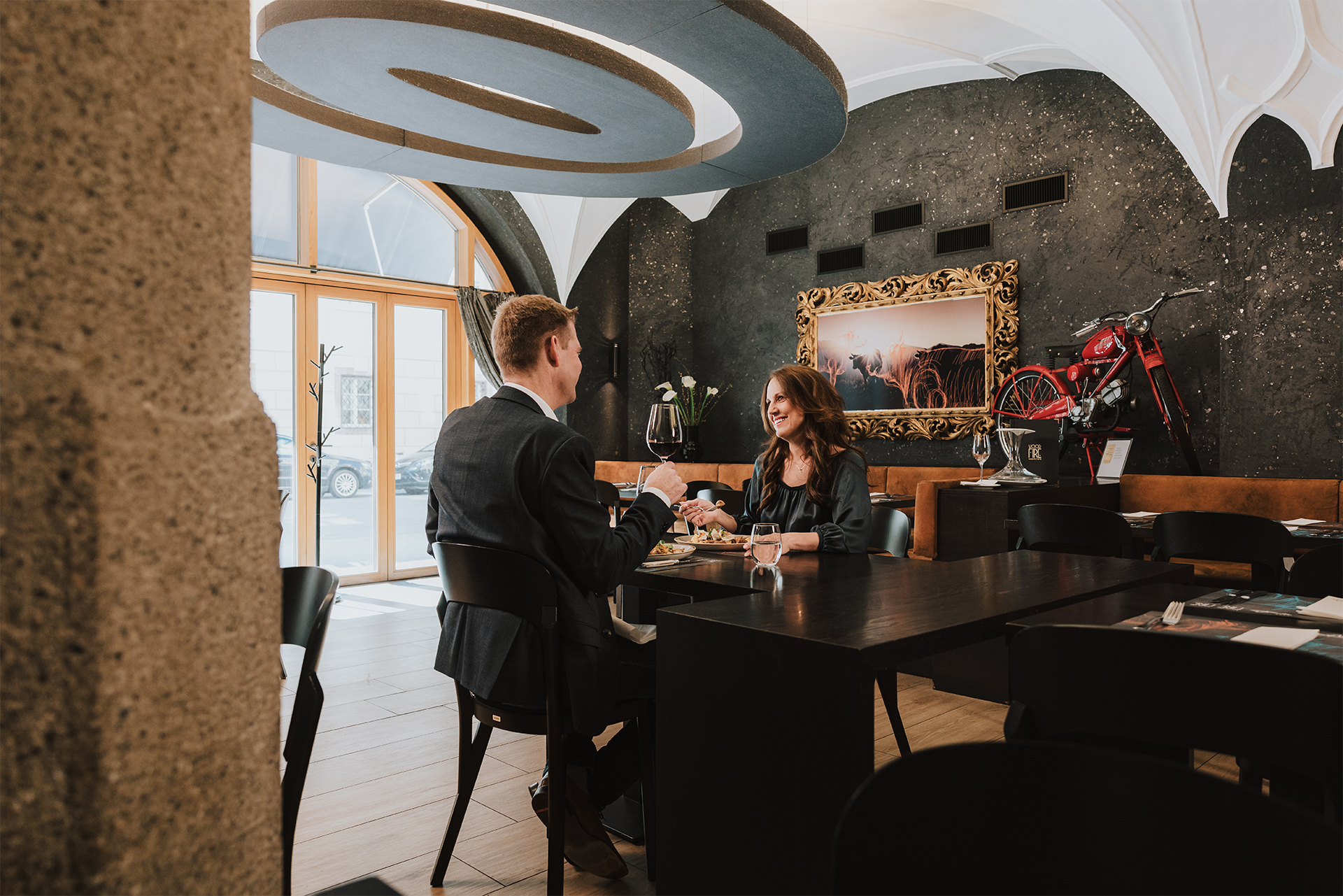 20250319-GrauerBaer_ohne_Grain-_N3A0524-©Roman-Huber Paar genießt Dinner im stilvollen Restaurant Woodfire des Grauer Bär Innsbruck Hotels, elegant dekoriert mit ausgefallenen Akzenten.